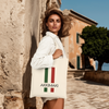 Woman carrying a stylish Italian-themed cotton tote bag with the text 'AKKIMAKI' on a scenic street.