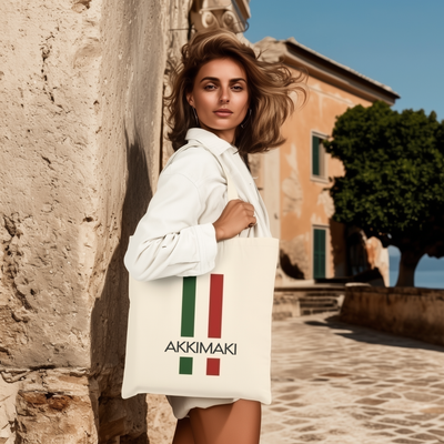 Woman carrying a stylish Italian-themed cotton tote bag with the text 'AKKIMAKI' on a scenic street.